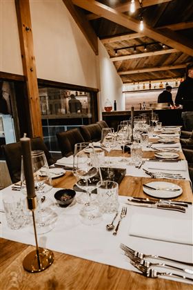 Ein elegant gedeckter Tisch in einem gemütlichen Restaurant. Die Atmosphäre ist warm und einladend, mit Holzdekor und schöner Tischdekoration.