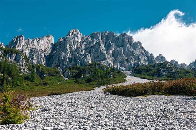 Eine beeindruckende Berglandschaft mit steilen Felsen und grünem Bewuchs. Der Himmel ist klar und blau, was die Landschaft noch beeindruckender erscheinen lässt.