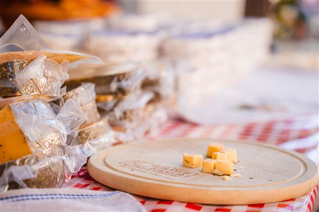 Eine Auswahl von verpacktem Käse auf einem Tisch mit einem Holzbrett im Vordergrund. Einige Käsewürfel liegen auf dem Brett.
