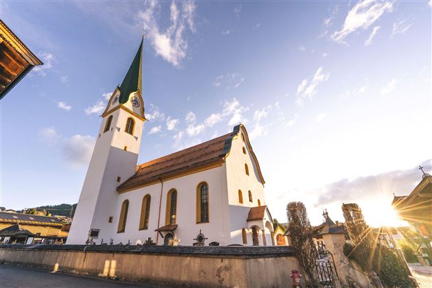 Eine schöne Kirche mit einem hohen grünen Dach und einem klaren Himmel im Hintergrund. Die Abendsonne beleuchtet die Fassade der Kirche.