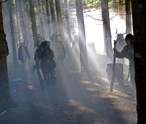 A dark forest scene with mysterious figures appearing between the trees. Rays of light break through the fog, creating an enigmatic atmosphere.