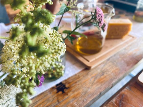 A tray with olive oil and cheese is on a wooden table. Fresh flowers are visible in the foreground.