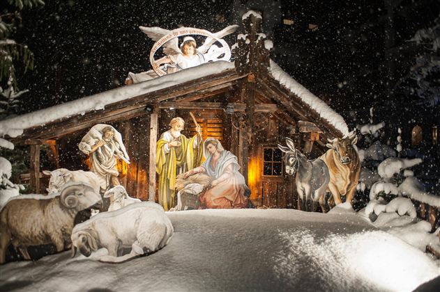 A wintry nativity scene with Mary, Joseph, and the newborn Jesus in a stable, surrounded by animals. Gentle snowflakes fall on the scene, creating a festive atmosphere.
