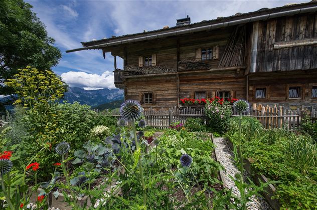 A man is carving a pumpkin with a tool. In the background, more pumpkins and straw bales are visible.