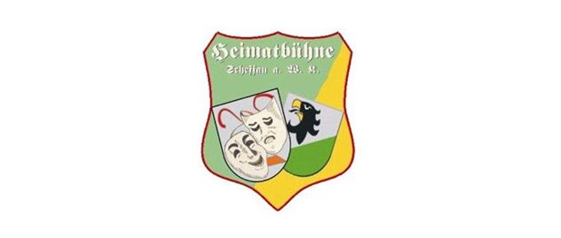 Een wapen met de tekst "Heimatbühne" en verschillende symbolen, waaronder een theatermaskermotief en een zwarte vogel. De kleuren zijn helder en in een schildontwerp gerangschikt.