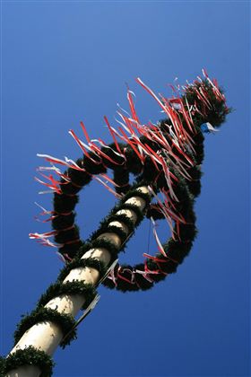Een versierde meiboom met kleurrijke linten voor een heldere blauwe lucht. De kleurrijke banden en de groene krans geven het een feestelijke sfeer.