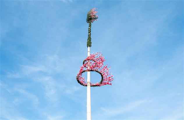 En udsmykket majtræ med farverige blomster og guirlander foran en blå himmel. Træet står højt og symboliserer foråret.