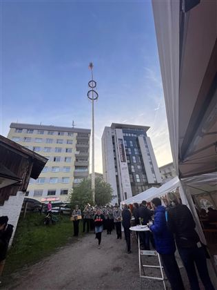 Oslava s davem lidí v městském prostředí. V pozadí je vidět vysoký sloup s prsteny.