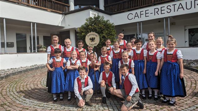 En gruppe børn i traditionelle dragter står foran en café-restaurant. De smiler glad og poserer til fotoet.