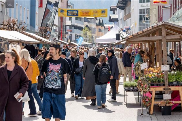 Ein belebter Markt mit vielen Menschen, die entlang der Stände schlendern. Die Atmosphäre ist freundlich und lebhaft.