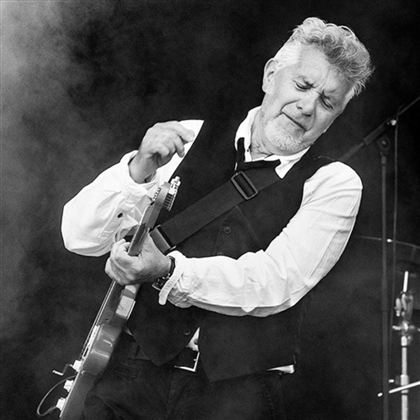 Ein Sänger spielt leidenschaftlich Gitarre auf der Bühne. Im Hintergrund sind verschwommene Lichter und Rauch zu sehen.