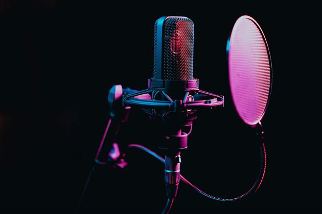 Ein Mikrofon mit einem Popfilter vor einem dunklen Hintergrund. Die Farben sind blau und lila beleuchtet.
