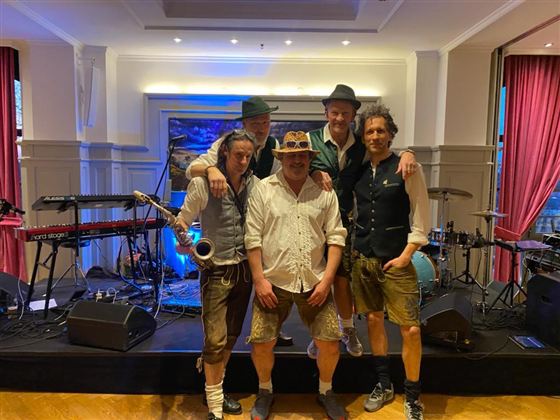 Eine Band steht auf der Bühne, umgeben von Musikinstrumenten. Sie tragen traditionelle Kleidung und posieren für das Foto.