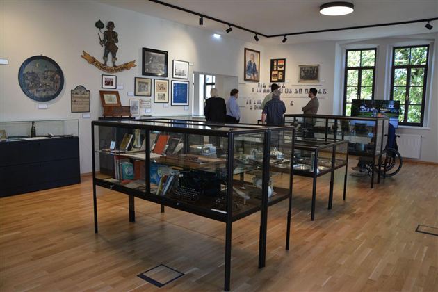 Ein Ausstellungsraum mit Vitrinen, die historische Gegenstände zeigen. Menschen betrachten die Exponate und die Wände sind mit Bildern und Tafeln dekoriert.