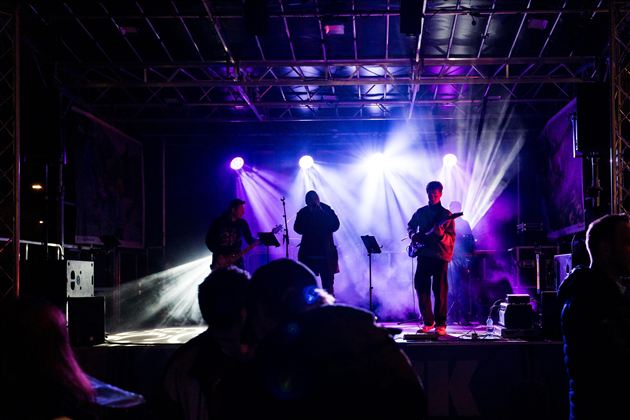Drei musizierende Figuren sitzen nebeneinander. Einer spielt das Akkordeon, einer die Violine und einer die Flöte.