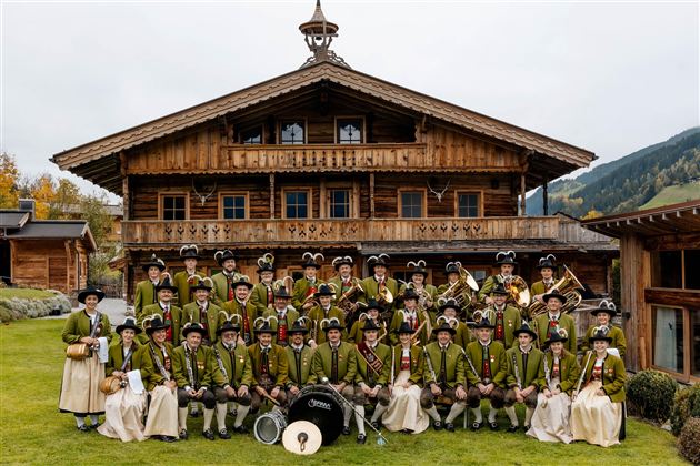 Dirigent řídí orchestr ve stanu. V pozadí jsou vidět hudebníci s nástroji.