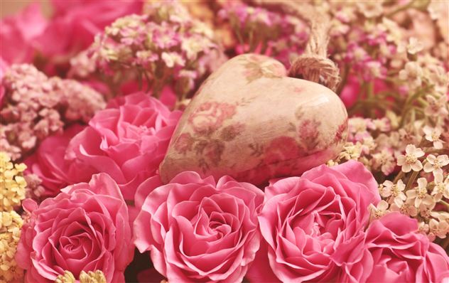 Ein hübsches Arrangement aus pinken Rosen und zarten Blumen. In der Mitte ist ein herzförmiger Anhänger zu sehen.
