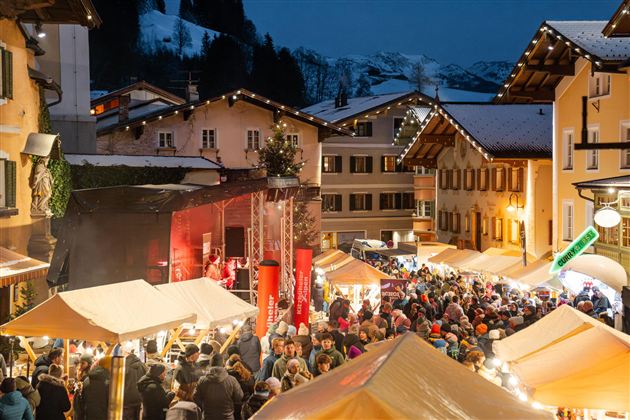Een drukke kerstmarkt op een winteravond. Veel mensen genieten van de feestelijke sfeer en de verlichte kraampjes.