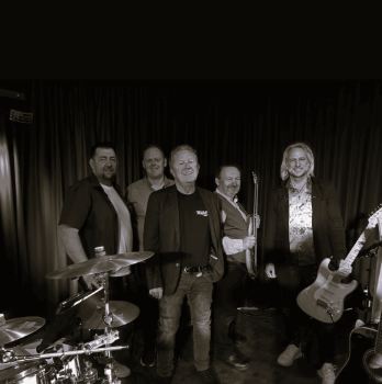 Een man ligt op de grond met een verbaasde gezichtsuitdrukking. Hij draagt elektroden en er liggen een reddingsring en een rode tas naast hem.