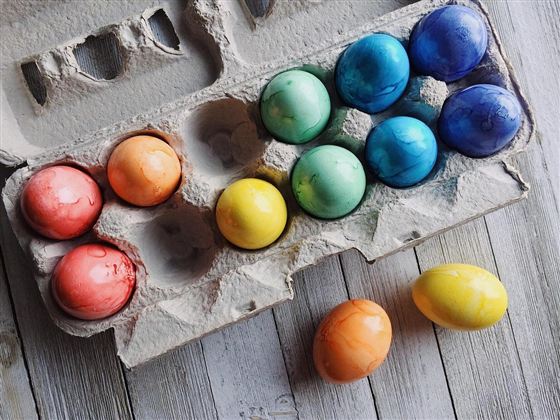 A box with colorful, hand-painted eggs in various colors. Some eggs are lying outside the box on a wooden surface.