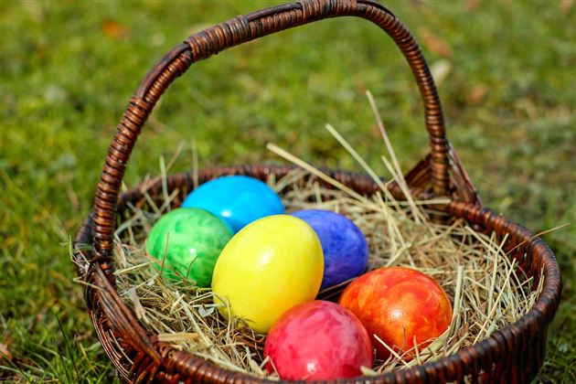 A basket with colorful Easter eggs lies on the grass. The eggs are in various colors like blue, yellow, red, and green.
