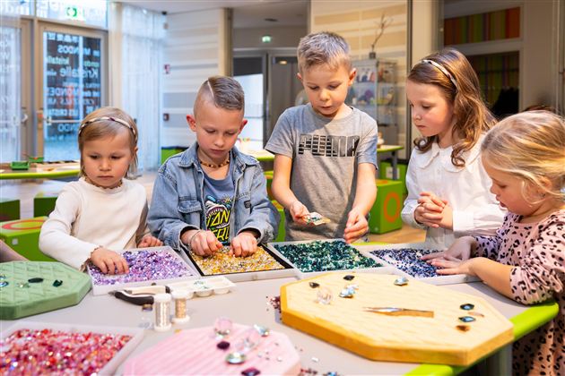 A group of children is working together on a craft project. They are sorting colorful beads and gems on a table.