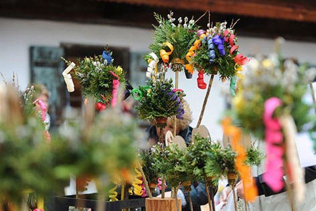 Colorful, decorated bouquets with flowers and colored ribbons are on a table. In the background, there are people and a traditional building.