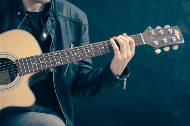 Ein Musiker spielt Gitarre. Er trägt eine schwarze Jacke und konzentriert sich auf das Instrument.