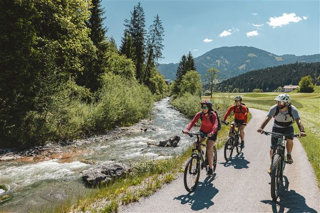 Ein natürlicher Felsen mit einer Öffnung, die einen Blick auf einen ruhigen See und Hügel gewähren. Der Himmel ist klar und blau.