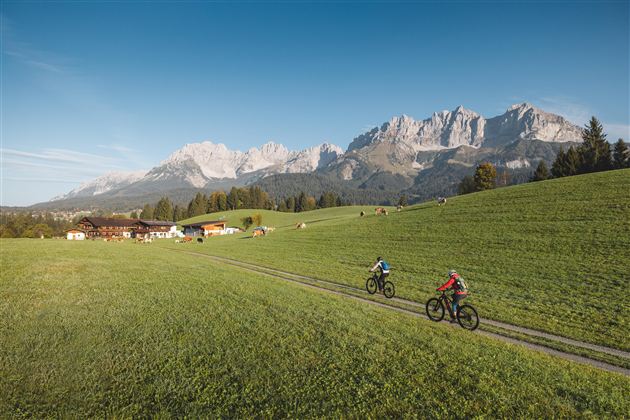 Een met sneeuw bedekte straat met hoge sneeuwmuren en een houten huis in de buurt. De lucht is helder en blauw met enkele wolken.