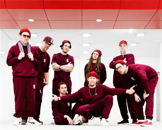 Eine Gruppe von acht Personen in roten Trainingsanzügen posiert in einem modernen Innenraum. Sie zeigen verschiedene Posen und haben Spaß zusammen.