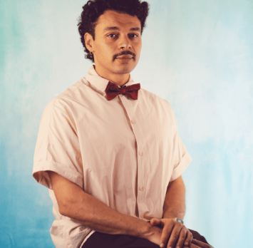 Een man ligt op de grond met een verbaasde gezichtsuitdrukking. Hij draagt elektroden en er liggen een reddingsring en een rode tas naast hem.