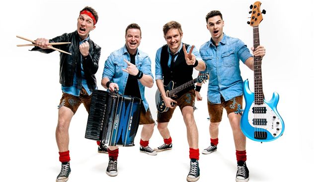 Eine fröhliche Band mit fünf Mitgliedern posiert in einer Action-Haltung. Sie tragen Trachtenlooks und halten verschiedene Musikinstrumente in der Hand.
