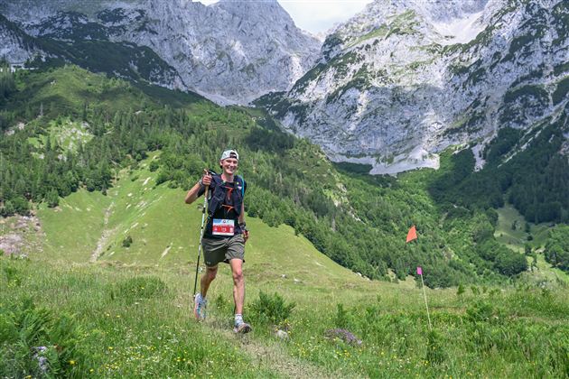 A runner wanders happily in a picturesque mountain landscape. High mountains and green meadows surround him.