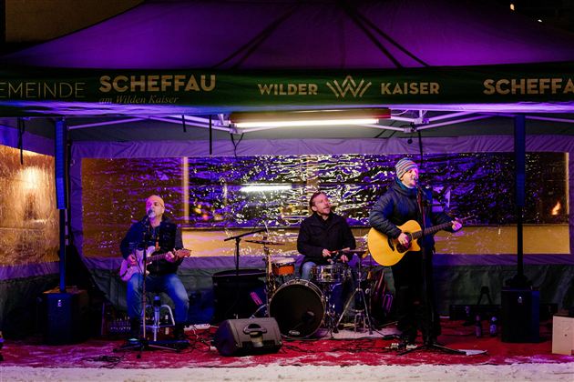 Eine Band spielt live unter einem Zelt in der Nacht. Die Atmosphäre ist festlich mit bunten Lichtern und einer schneebedeckten Umgebung.
