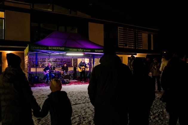 Eine Live-Musikaufführung unter einem Zelt in der Nacht. Die Zuschauer stehen im Schnee und genießen die Musik.