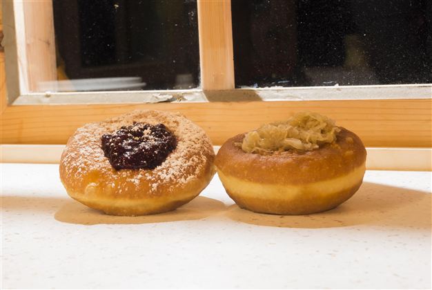 Zwei leckere Donuts auf einem Tisch. Der linke Donut hat eine Füllung aus Marmelade und Puderzucker, der rechte ist mit einer cremigen Füllung.