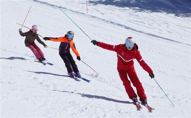 Three skiers are riding in a snowman under a sunny sky. They are wearing colorful ski clothes and enjoying winter sports.