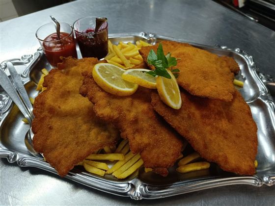 Ein großer Teller mit knusprigem Schnitzel, serviert mit Pommes frites und zwei verschiedenen Dips. Frische Zitronenscheiben und ein Minzblatt verleihen dem Gericht eine dekorative Note.