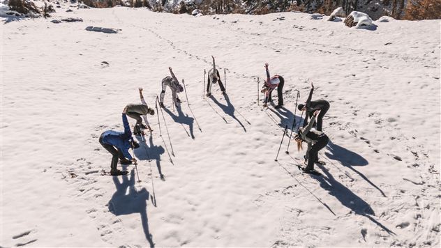 Eine Gruppe von Skifahrern übt im Schnee. Sie sind in einer offenen Winterlandschaft mit Sonne und Bäumen im Hintergrund.