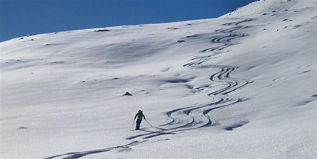 Ein Skifahrer fährt durch den frischen, unberührten Schnee. Der Himmel ist klar und blau, und die Berge bilden eine schöne Kulisse.