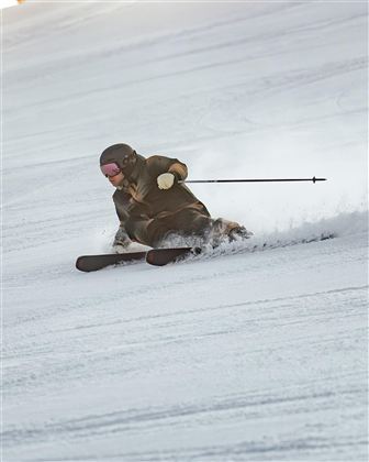 Ein Skifahrer fährt schnell den Hang hinunter und macht eine Kurve im Schnee. Die Umgebung ist weiß und winterlich.