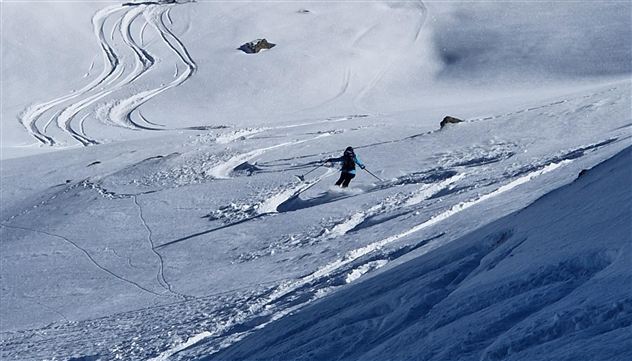 Ein Skifahrer fährt auf unberührtem Schnee in einer Berglandschaft. Die Spuren im Schnee zeigen die Abfahrt und verleihen der Szene Dynamik.