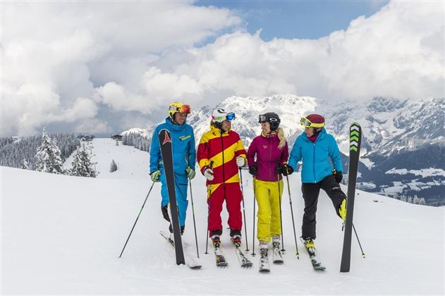 A group of four skiers is standing on a snow-covered slope. In the background, there are mountains and a cloudy sky.
