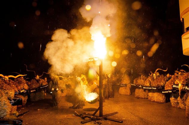 Een feestelijke scène met mensen in levendige kleding die om een vuur verzameld zijn. Rook en lichten creëren een opwindende sfeer in de duisternis.