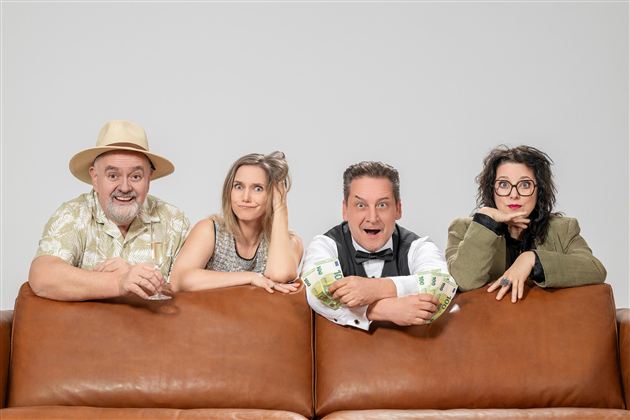 Eine Gruppe von vier Personen sitzt auf einer Couch. Sie zeigen verschiedene Gesichtsausdrücke und wirken unterhaltsam und gespannt.