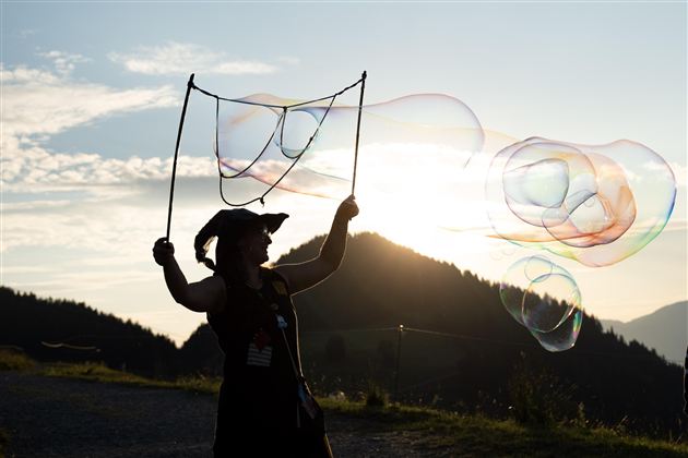 Eine Person steht im Sonnenuntergang und bläst Seifenblasen. Die Berge und der Himmel sind im Hintergrund gut sichtbar.