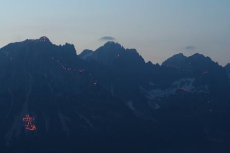 Die Berge sind im Dämmerlicht mit Feuer gekennzeichnet. Ein großes Kreuz leuchtet an der Hangseite.