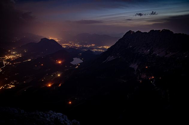 A breathtaking mountain landscape at night with glowing city lights in the valley. The sky displays soft hues of twilight.