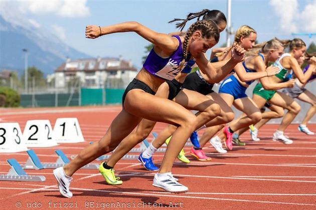 Eine Gruppe von Athletinnen startet bei einem Wettlauf auf einer Laufbahn. Die Sportlerinnen zeigen viel Dynamik und Konzentration.